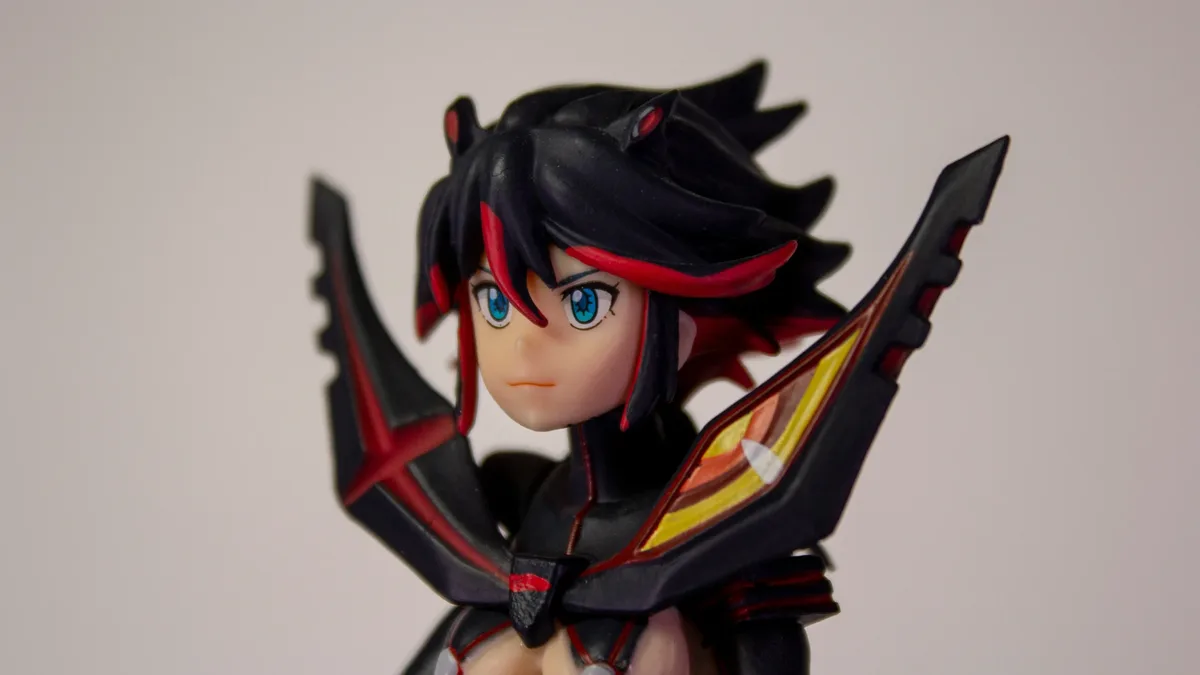 A close-up of a figurine of a female anime character with black hair and red accents, wearing a black outfit with red and yellow details.